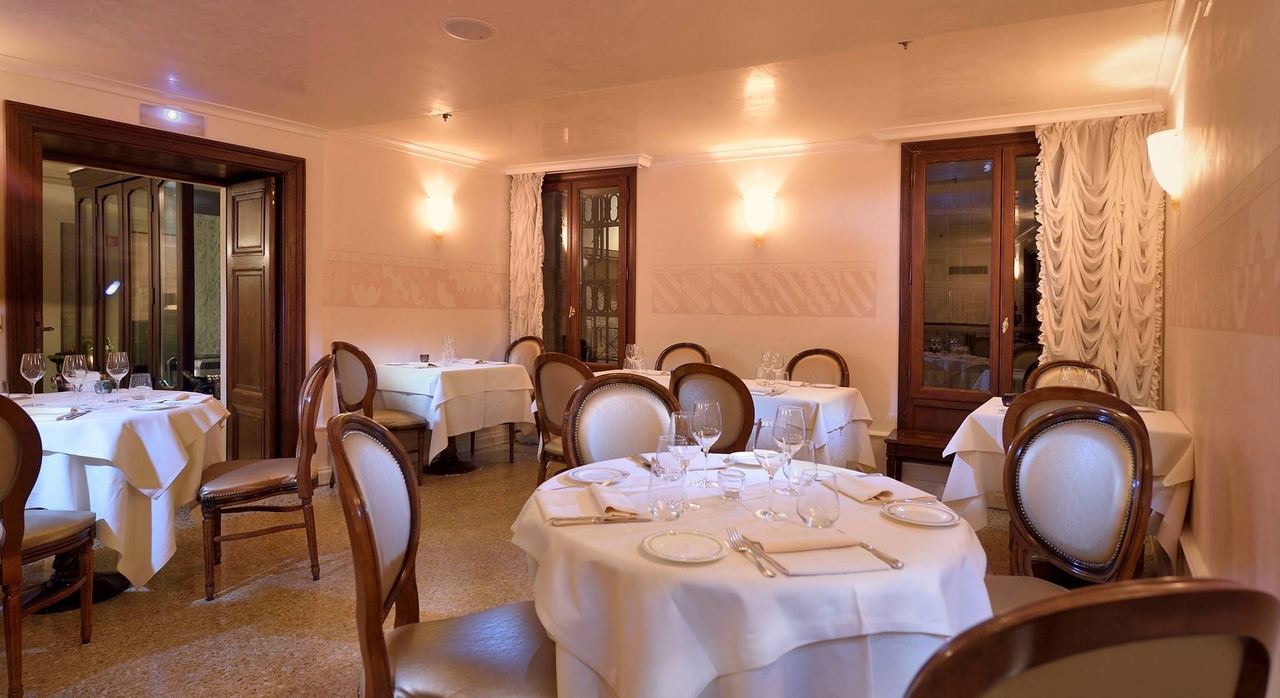 The dining room of Alle Corone, with round tables laid in white