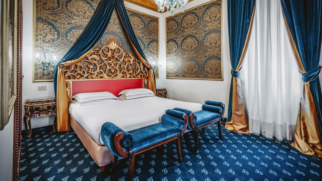 A bedroom at Hotel Giorgione, with a gilded carved headboard and blue silk drapes