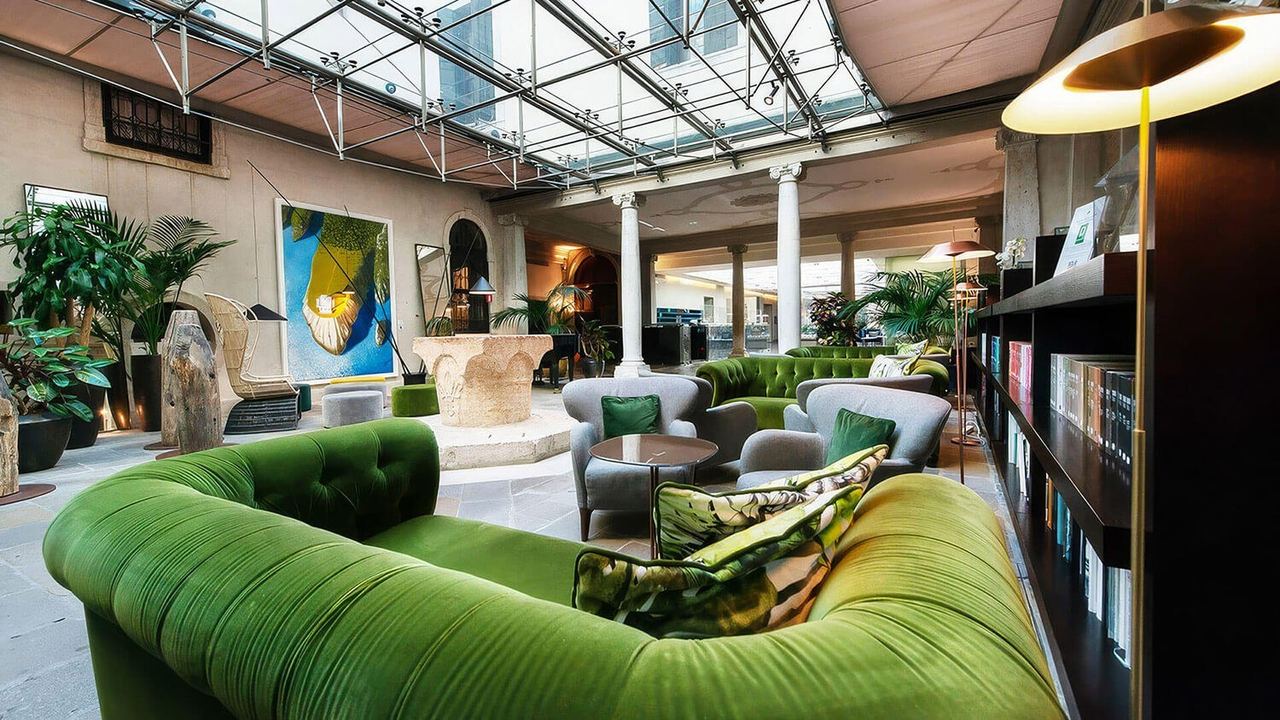 The glass-roofed lounge of Hotel Monaco & Grand Canal, with green velvet sofas around a stone wellhead