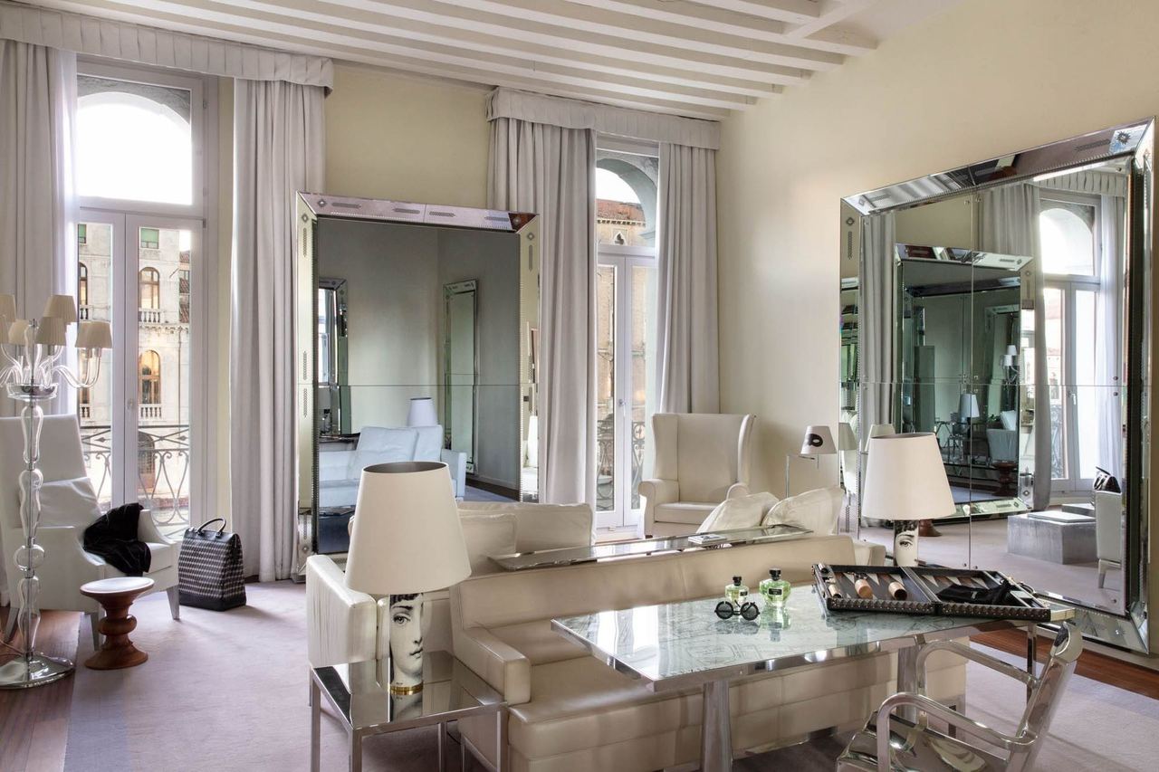 A white sitting room at Palazzina Grassi, with tall mirrors and windows on the canal
